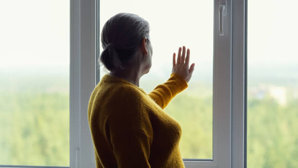istock Mature woman missing old time touches window with hand 1674441063