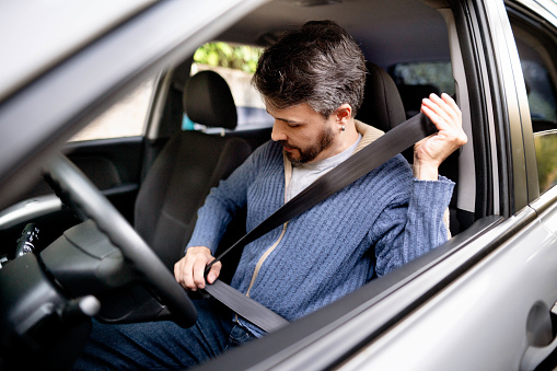 Man sitting in his car and putting on his seat belt before going for a drive