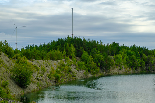 This is a former shale quarry with azure water and picturesque hills. Unlike the Narva shale settling ponds. A dark autumn day. Estonia, Aidu quarry. A tall wind turbine in the distance.