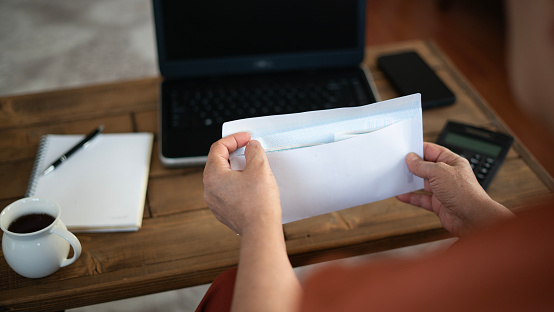 Adult woman opening tax envelope while working on laptop at home