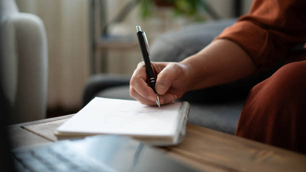 istock Close-up Adult woman taking notes while working on laptop at home 1674494150