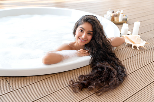 Beautiful Indian girl showing her long hair while lying in round bath with foam.