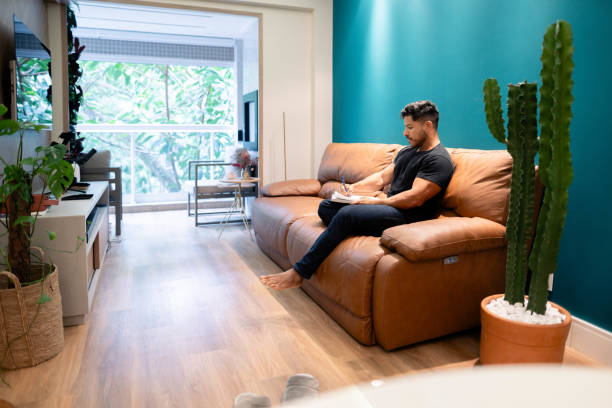 istock Young man writing in a dairy sitting on living room couch 1674500747