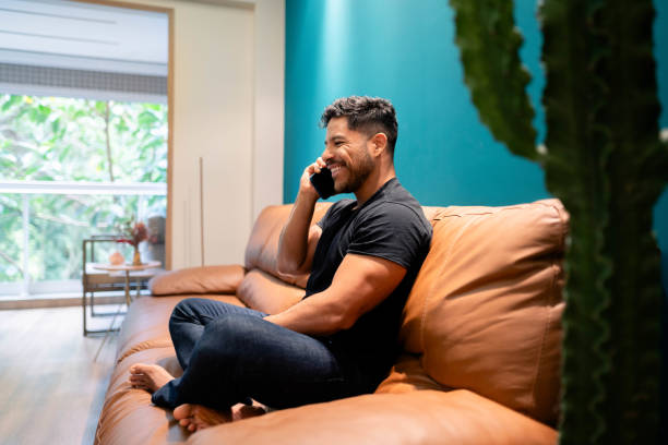 istock Young man talking on mobile phone sitting on living room couch 1674500762
