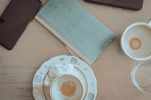 Two empty coffee cups, book and mobile phones on wooden table. Breakfast table. Morning drinks. Cafe interior. Urban lifestyle. Coffee break background. Daily life. Flat lay.