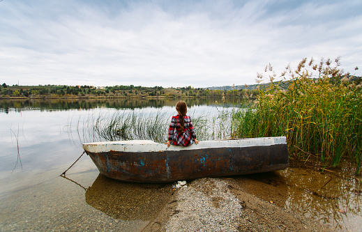 Rear view of child sitting in a boat and looking at the beautiful lake view