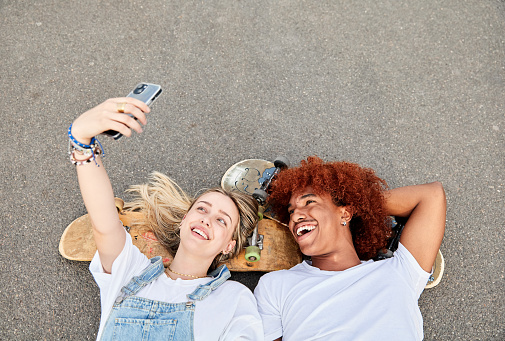 Top view of friends taking selfie lying on skate park using the skateboard as pilow. Concept of friendship and generation z.