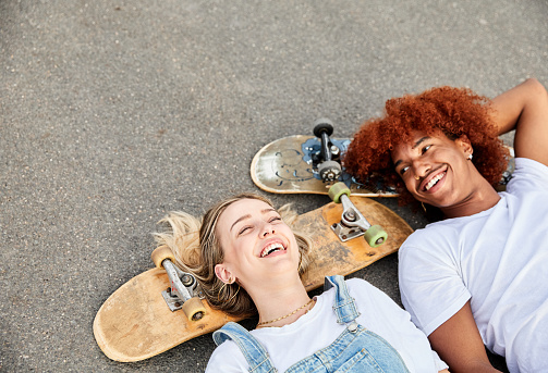 Photo with copy space and top view of two happy multiracial skateboarders lying on a road. Concept of friendship and generation z.