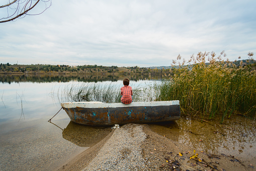 Rear view of boy sitting in a boat and looking at the beautiful lake view