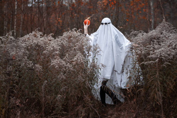 istock Woman in Halloween ghost costume throws pumpkin bomb 1674534394