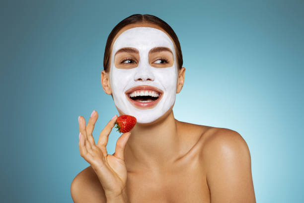 Happy young girl with facial mask and strawberry stock photo
