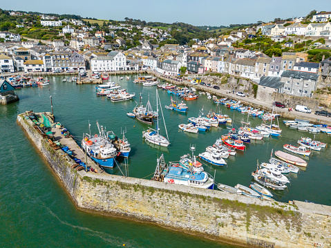 Mevagissey, UK. 5 September 2023. Boats in Mevagissey Harbour, shops of the town and people on the quay in Cornwall.