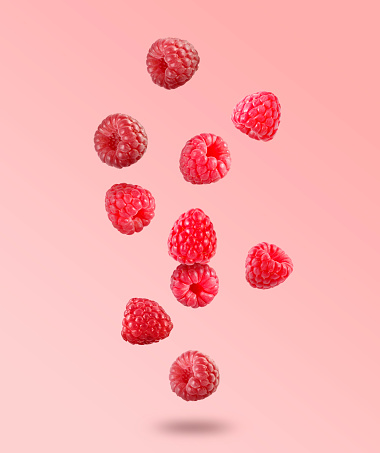 Many fresh ripe raspberries falling on pink background