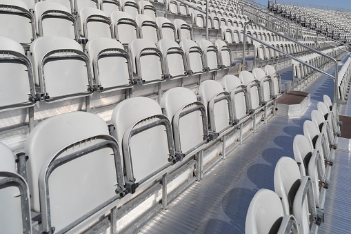 Rows of blue and grey empty plastic seats on the stands of a sports stadium on a summer day