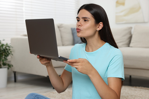 Young woman having video chat via laptop and blowing kiss at home