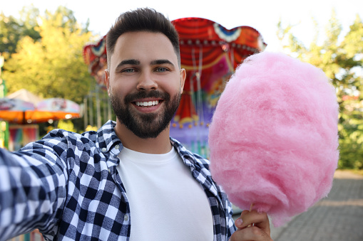 Happy young man with cotton candy taking selfie at funfair