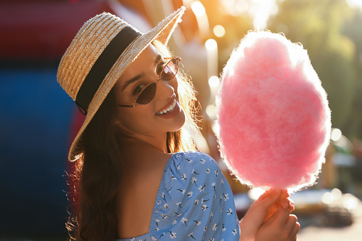 Beautiful young woman with cotton candy outdoors on sunny day