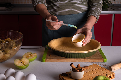 Woman spreading eggs on the dough with a cooking brush in a bakery dish, apple pie making, Thanksgiving tart preparation, autumn bakery, lifestyle, Crispy weather sweets, recipe