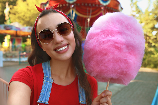 Stylish young woman with cotton candy taking selfie at funfair