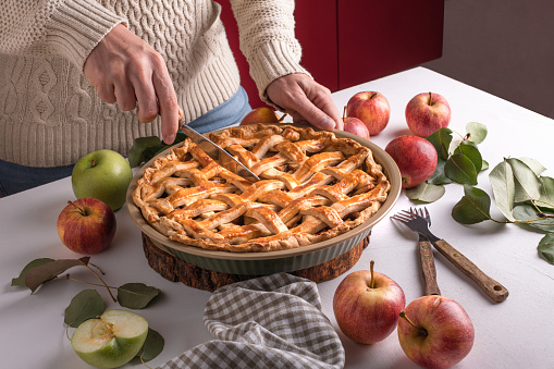 Woman cutting a baked apple with a khife, Thanksgiving traditional dessert ready to eat with red and green apples, Thanksgiving tart preparation, autumn bakery. Crispy weather sweets. Recipe