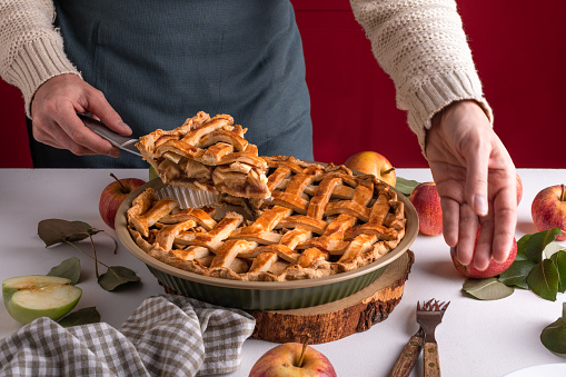 Woman serving a slice of apple pie on a plate, ready to eat. Thanksgiving traditional dessert with red and green apples, Thanksgiving tart preparation, autumn bakery. Crispy weather sweets, recipe