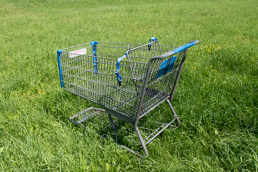 An abandoned shopping cart is standing alone is a field of grass.