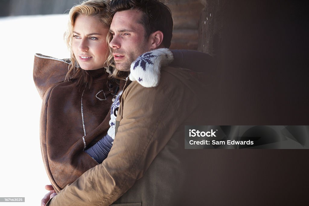 Sonriente pareja abrazándose en la nieve - Foto de stock de Cabaña de madera libre de derechos