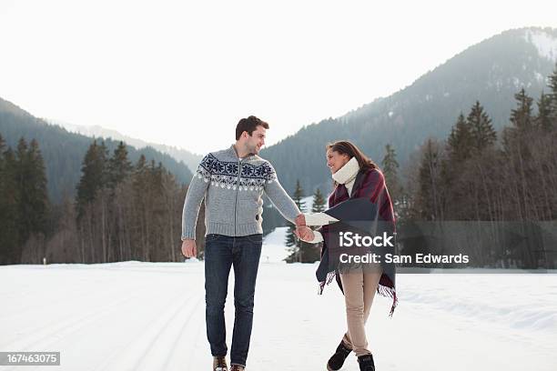 Smiling Couple Holding Hands And Walking In Snowy Field Stock Photo - Download Image Now