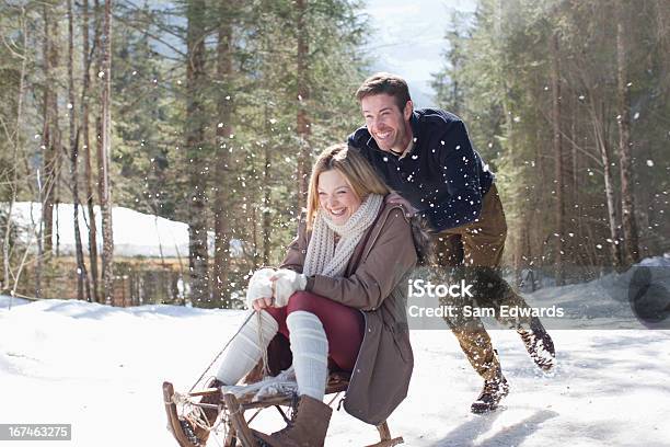 Smiling Couple Sledding In Snow Stock Photo - Download Image Now - Fun, Vacations, Winter