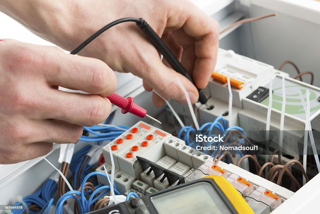 Hands of an electrician working on a circuit Hands of an electrician with multimeter probe at an electrical switchgear cabinet Control Panel Stock Photo