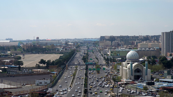 The cityscape of Tehran with the view of the cars moving on multiple lanes of a highway alongside a Mosque viewed from the top of the Azadi tower in Tehran, Iran on July 20th, 2023