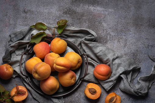 Sweet, juicy, ripe apricots in a metal bowl on a gray background. Whole fruits, halves of apricots, fruits with leaves