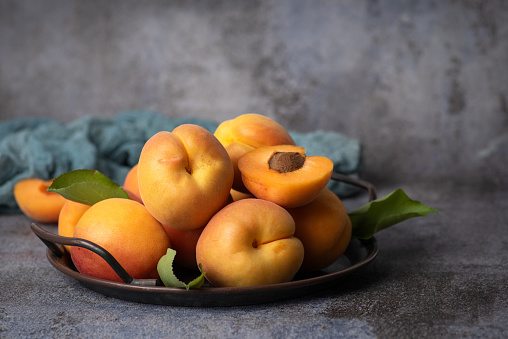 Sweet, juicy, ripe apricots in a metal bowl on a gray background. Whole fruits, halves of apricots, fruits with leaves