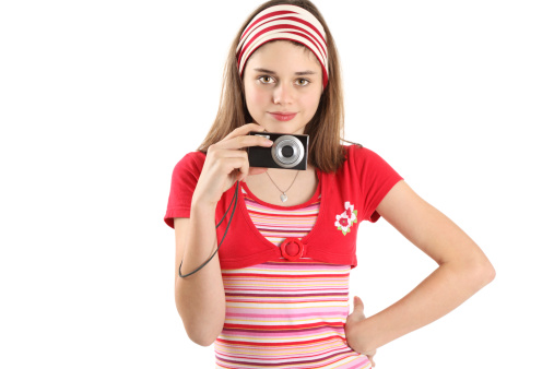 Smiling teenage girl holding camera in front of white background