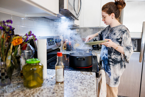 Brunette Caucasian woman in eyeglasses cooking and boiling vegetables in a pot in kitchen
