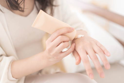A Japanese woman is sitting on the bed and applying hand cream to her hands.