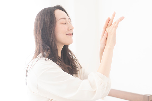 A Japanese woman is sitting on a sofa and applying hand cream to her hands.Smell the nice scent of hand cream and feel happy.