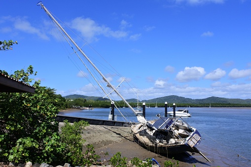 Cooktown, Qld - July 12 2023:Sailboat boat stranded on riverbank beach after a storm.In 2021 there were 45 capsizing incidents reported in Queensland Australia, with two of these incidents each resulting in a fatality.