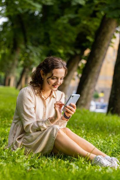 istock Smiling young woman using smartphone typing text answering messages chatting online in city park 1674955365