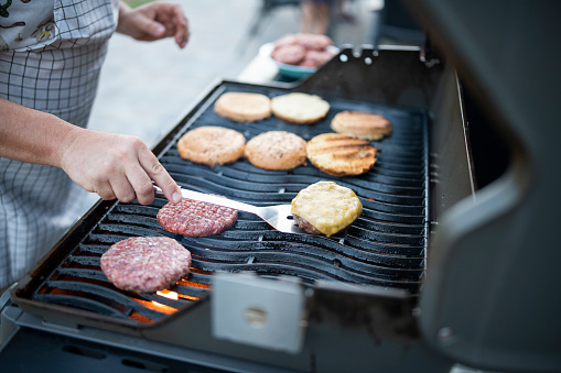 Mid adult man preparing delicious looking homemade burgers on a grill in the back yard at a garden party.