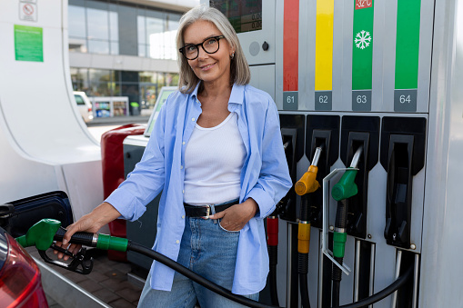 Beautiful young woman text messaging on smart phone while refueling gas tank at fuel pump