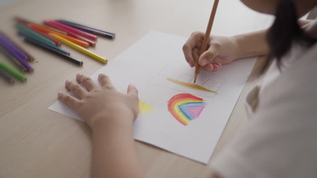 A girl enjoys coloring and drawing on a paper at home. Kid with paint arts