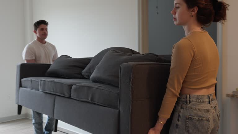 Young couple moving sofa in new rental apartment. Caucasian brunette woman with Hispanic man with mustache transforming room and settling down