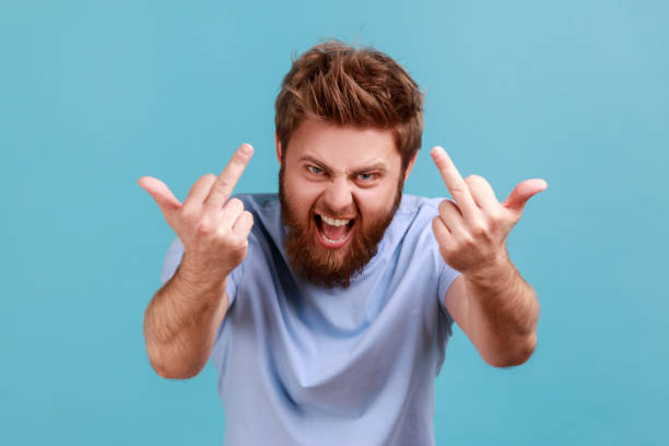 Man in blue T-shirt showing middle fingers, impolite rude gesture of disrespect, fuck off expression stock photo