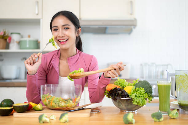 An attractive Asian woman in sportswear enjoys her healthy salad at a kitchen table in the kitchen. An attractive and cheerful Asian woman in sportswear enjoys her healthy salad at a kitchen table in the kitchen. Healthy lifestyle concept Exercise  stock pictures, royalty-free photos & images