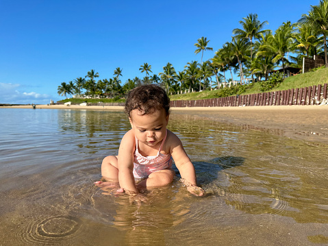 Baby playing with sand in the sea on a beach with coconut trees