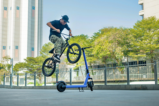 Young bmx rider jumping over scooter as barrier in the city, BMX freestyle in a skate park.