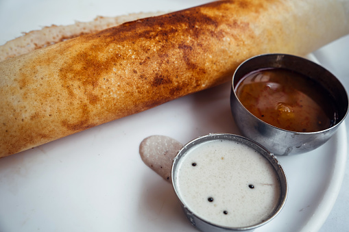 Dosa Ghee roast Dosa, famous south Indian breakfast item which is made in caste iron pan in traditional way and arranged on a white base with side dish ,on a white background.