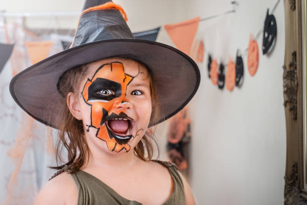Portrait of a child with a drawing mask on her face and hat in Halloween decorations