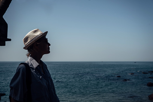 A tourist girl in dark glasses and a white hat against the background of the boundless blue sea. A picture about traveling to the sea in blue tones.